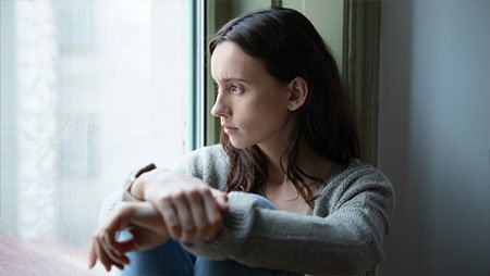 Девушка напряженно сидит возле окна